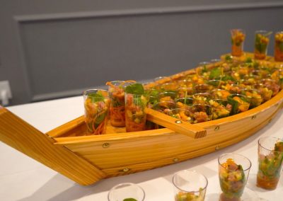 A miniature wooden boat with food in small cups.